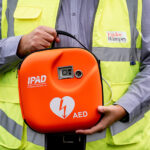 Housebuilder donates defibrillator to Penicuik primary school Construction worker holding defibrillator