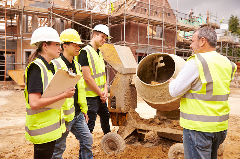 Builder using cement mixer on site with apprentices
